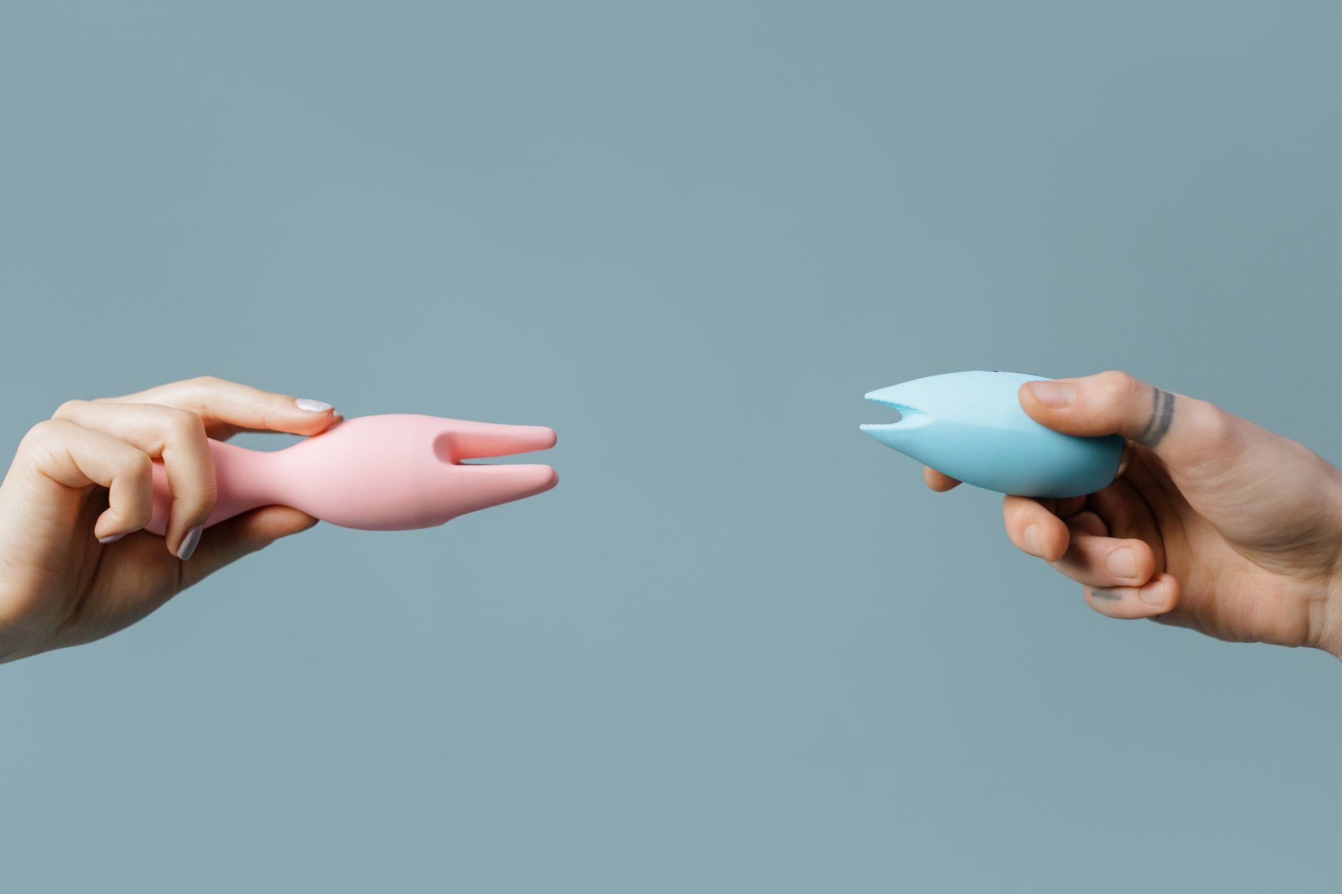 Two hands holding colorful silicone vibrators in intimate setting