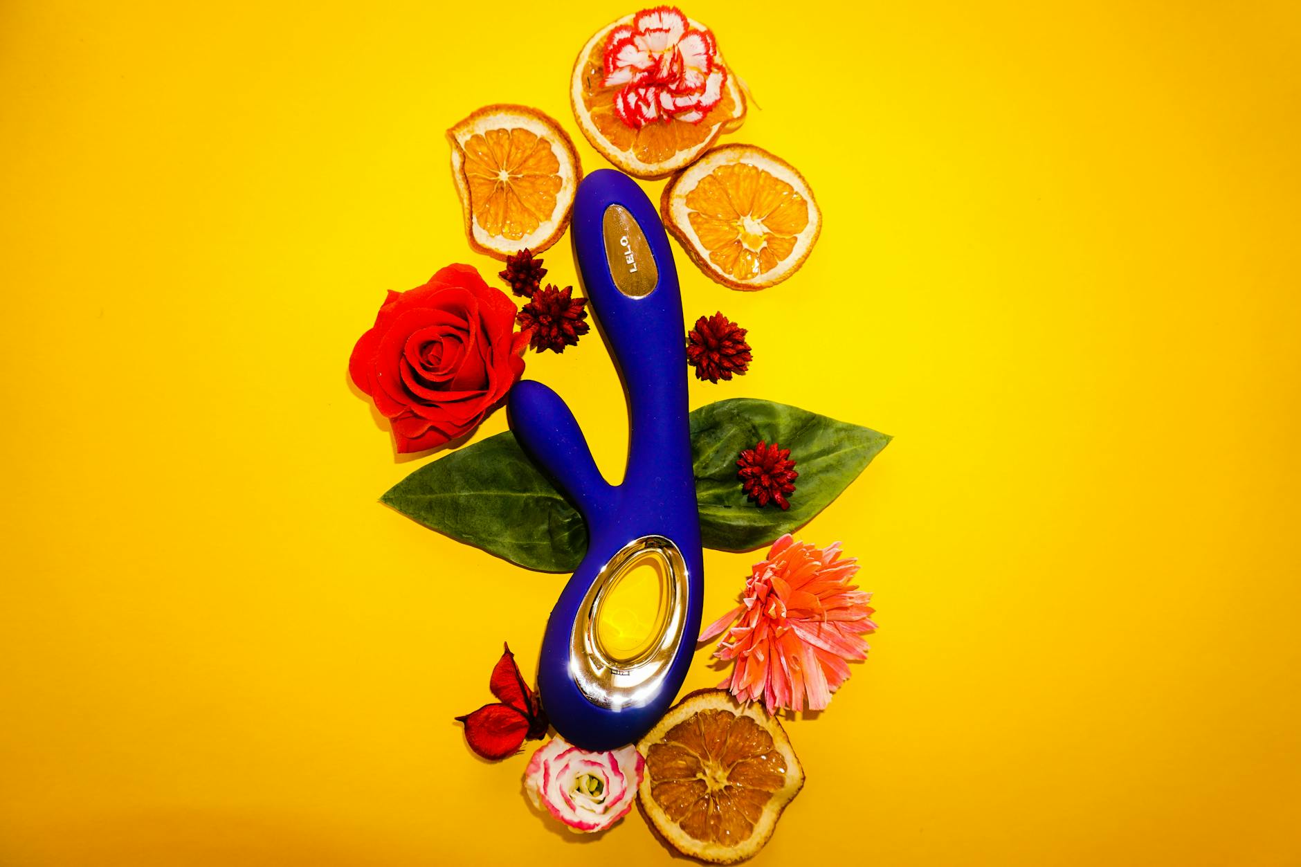 A blue vibrator surrounded by fresh lemons and citrus on a bright yellow background
